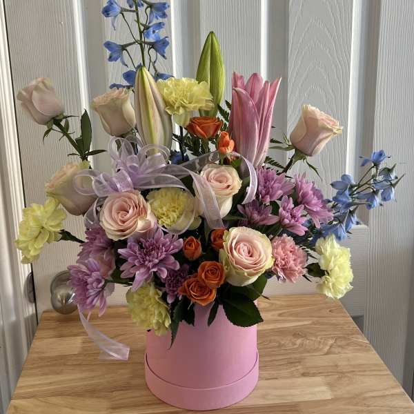 Mixed bouquet in a pink hatbox with roses, lilies, chrysanthemums, and blue delphinium
