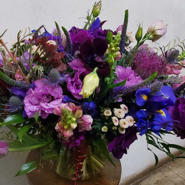 Large mixed bouquet of purple, pink, and blue flowers in a glass vase