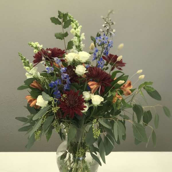 Mixed bouquet of burgundy, white, and blue flowers in a glass vase