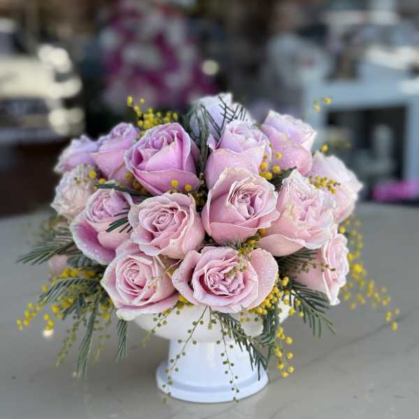 Pink roses arranged in a white pedestal vase with yellow filler flowers