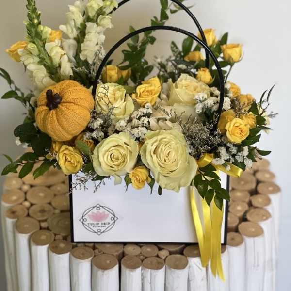 Yellow and cream roses arranged in a white gift box with a small knitted pumpkin
