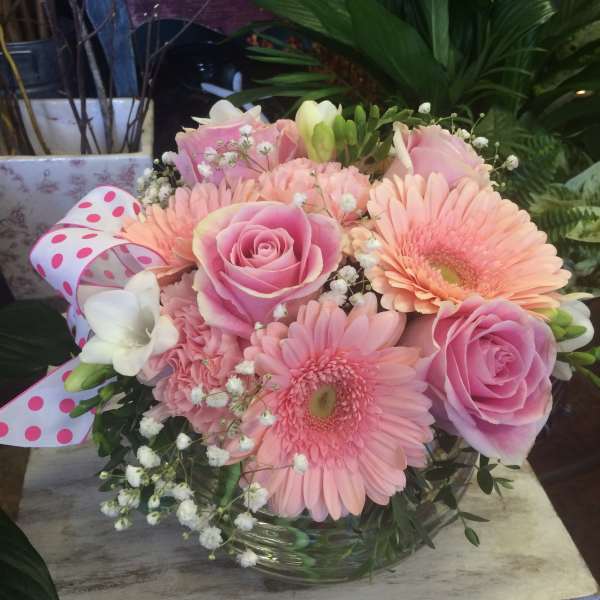 Pink roses and gerbera daisies in a glass vase with a polka-dot ribbon