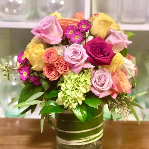 Mixed bouquet of pink, yellow, and orange roses in a glass vase