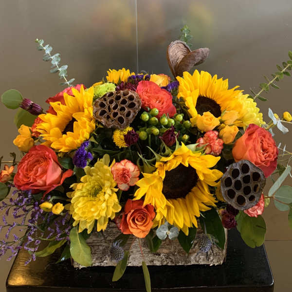 Bright mixed bouquet with sunflowers, roses, and lotus pods in a rustic container