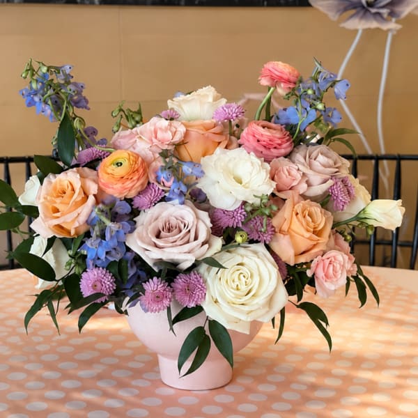 Pastel bouquet of roses, ranunculus, and blue flowers in a pink vase