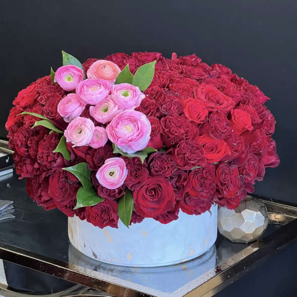 Round arrangement of red and pink flowers in a white box