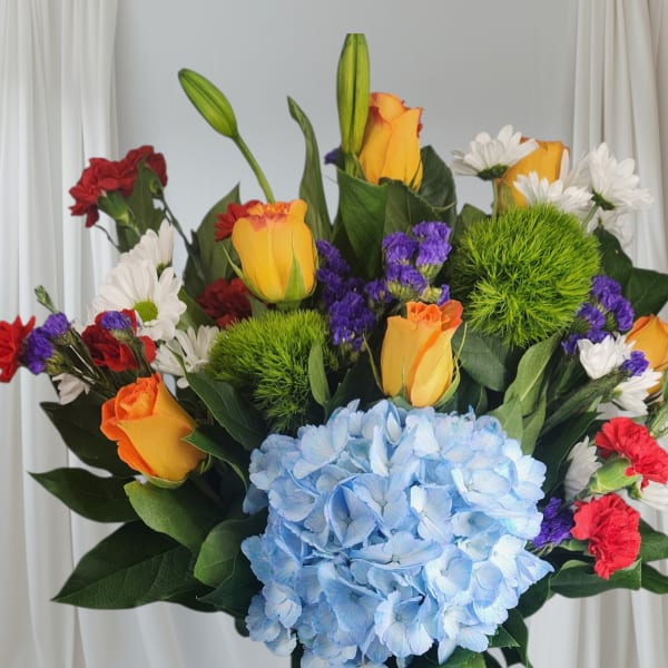 Colorful bouquet with blue hydrangea, roses, carnations, and daisies in a blue vase