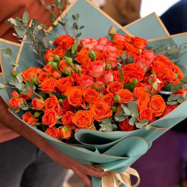 Bouquet of orange and pink roses wrapped in teal paper
