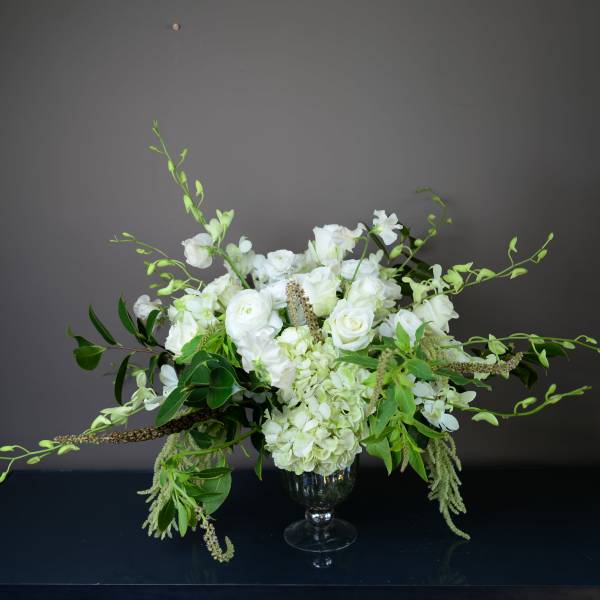 White floral arrangement in a glass vase with trailing greenery
