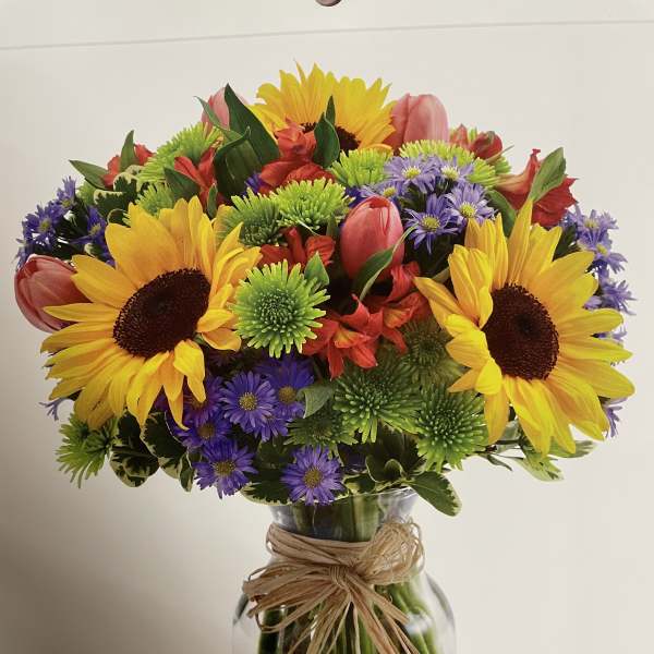 Bright mixed bouquet with sunflowers, tulips, and purple daisies in a glass vase