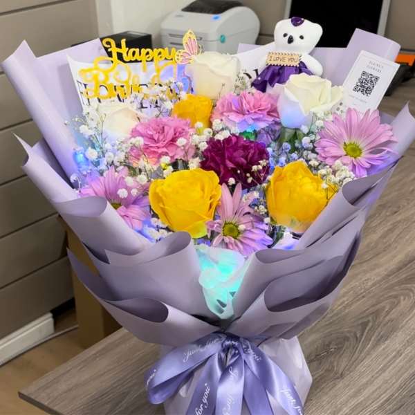 Bouquet of yellow and pink roses with daisies in lavender wrap