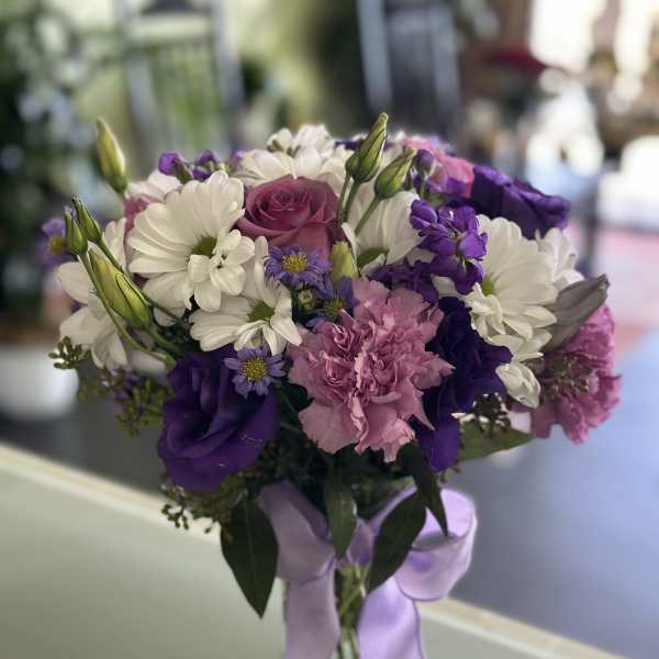 Bouquet of white daisies, purple blooms, and pink carnations in a glass vase