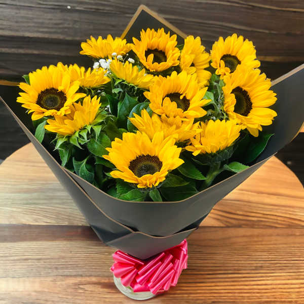 Bouquet of yellow sunflowers wrapped in black paper with a pink ribbon