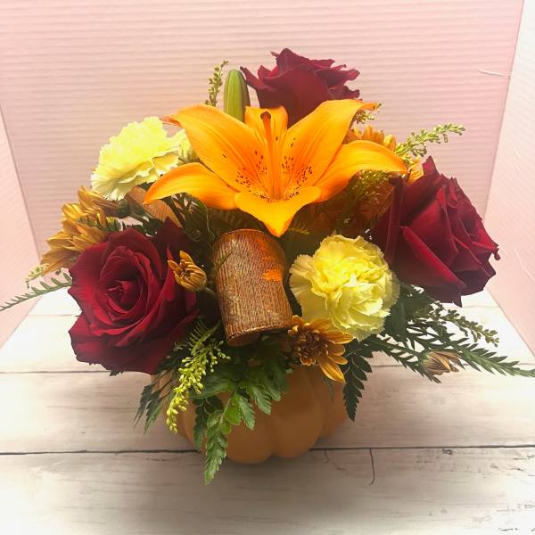 Bouquet of red roses, orange lily, and yellow carnations in a pumpkin container