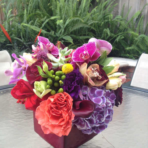 Colorful mixed bouquet in a burgundy vase with orchids, roses, and hydrangeas