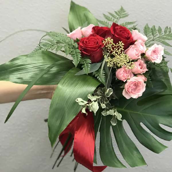 Bouquet of red and pink roses with large tropical leaves