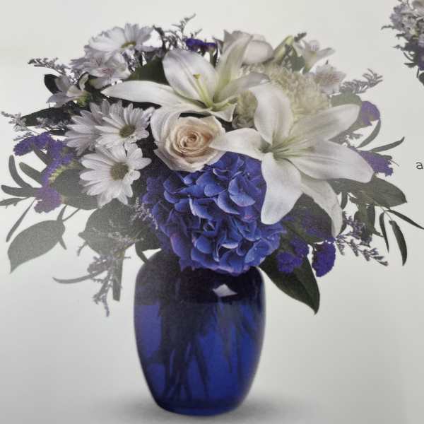 White lilies and purple flowers arranged in a blue glass vase