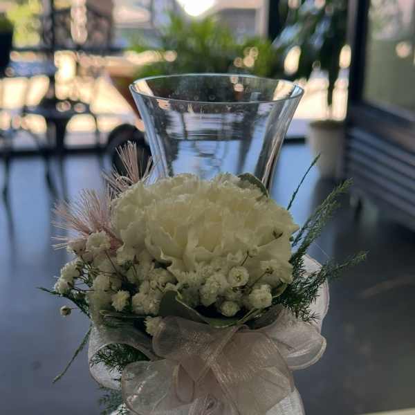 White floral arrangement in a clear glass vase with a sheer ribbon bow