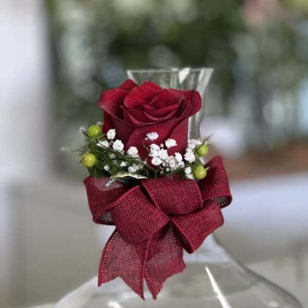 Clear glass vase with a single red rose, white filler flowers, green berries, and a red bow at the neck.