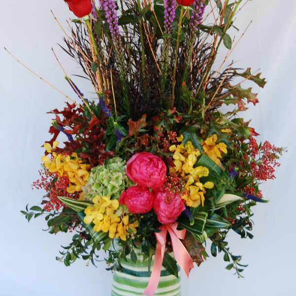 Tall arrangement of red roses, pink blooms, and yellow flowers in a striped vase