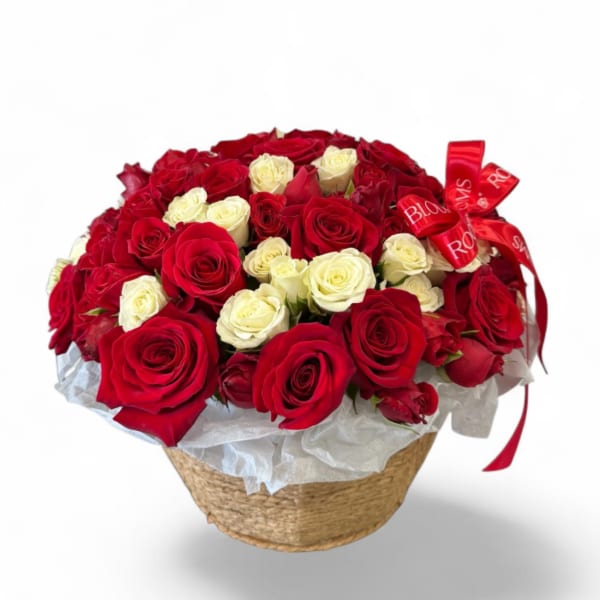 Red and white roses arranged in a woven basket with a red ribbon