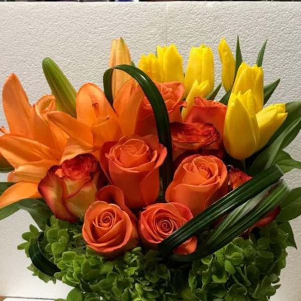 Orange roses and yellow tulips arranged in a glass vase
