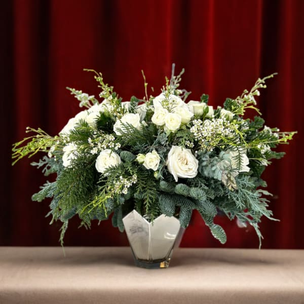 White roses in a glass vase with dense evergreen foliage