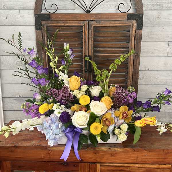 Mixed flower arrangement with roses, orchids, and purple blooms in a white container