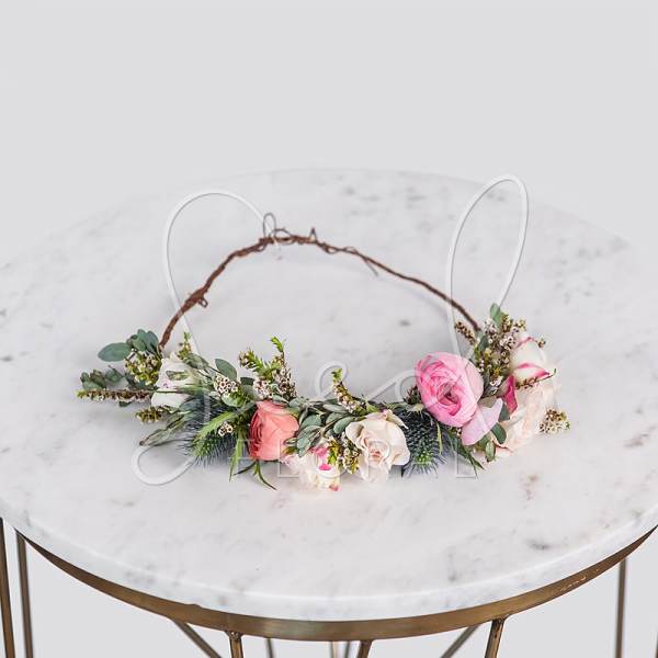 Delicate floral crown with pink and white roses arranged along a vine base on a marble table.