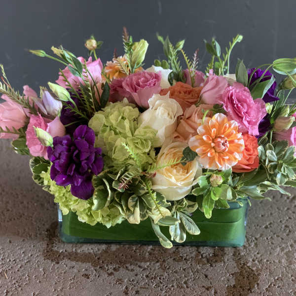 Mixed bouquet in a green glass vase with pink, purple, peach, and white flowers
