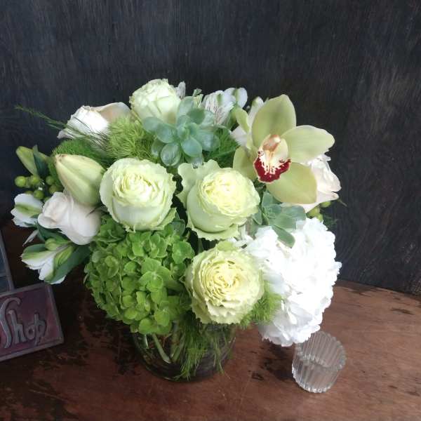 Green and white floral arrangement in a glass vase with orchids and roses