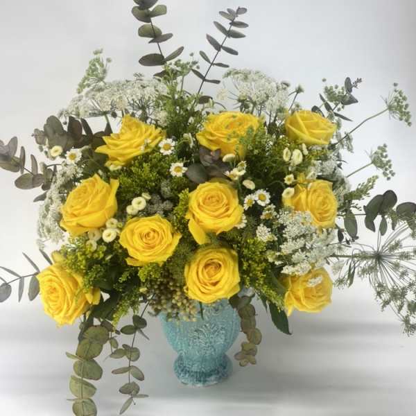 Yellow roses in a turquoise vase with airy white filler flowers
