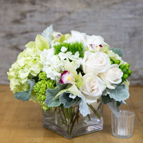 White and green floral arrangement in a square glass vase