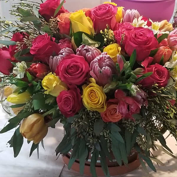 Mixed bouquet of pink and yellow roses with assorted blooms in a round container
