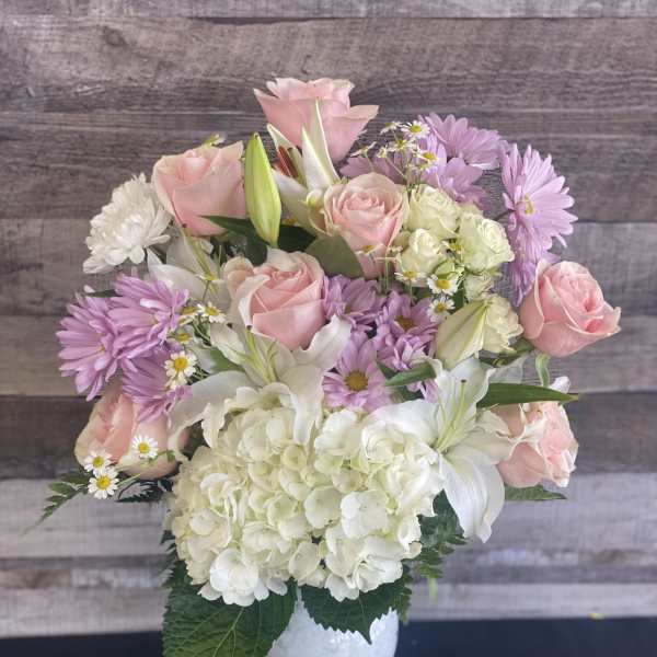 Pink roses, white lilies, and lavender daisies in a white vase
