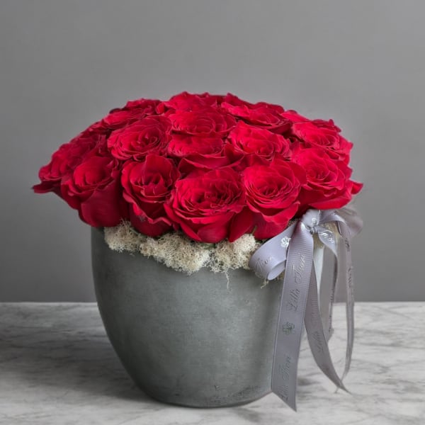 Red roses arranged in a gray pot with a ribbon bow