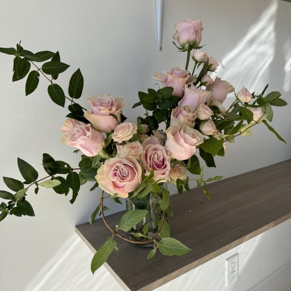 Pink roses arranged in a clear glass vase with trailing greenery