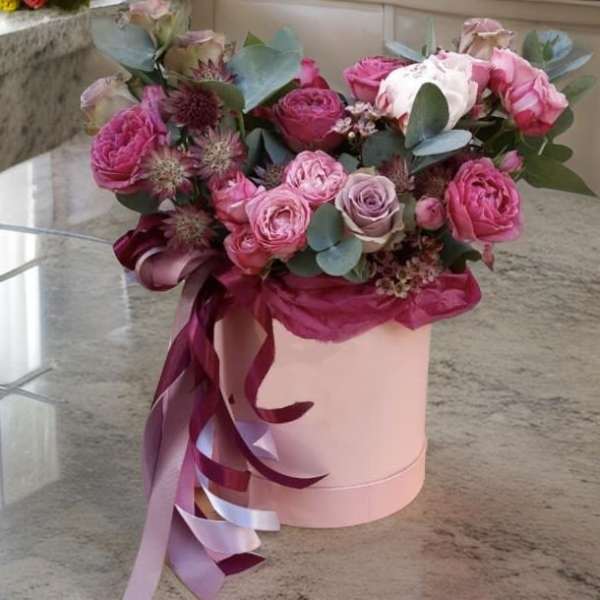 Pink and lavender roses in a round hatbox with ribbon