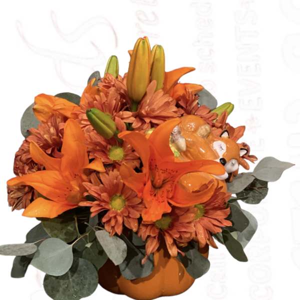 Orange lilies and mums arranged in a pumpkin-shaped container with a fox accent
