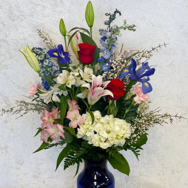Mixed bouquet of roses, lilies, irises, and hydrangeas in a blue vase
