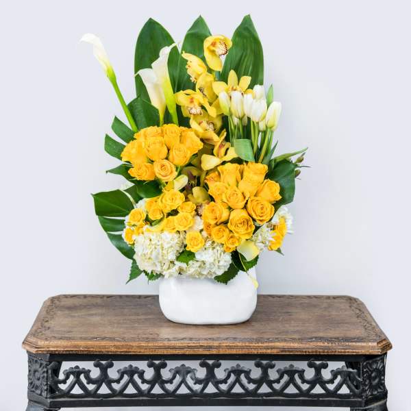 Yellow roses and white calla lilies arranged in a white vase