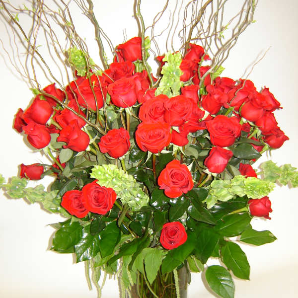 Red roses arranged in a clear glass vase with curly branches