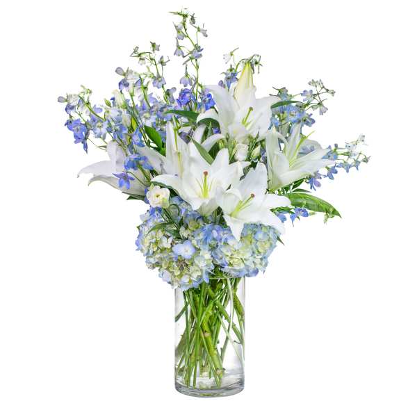 White lilies and blue flowers arranged in a clear glass vase