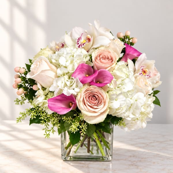 Bouquet of white hydrangeas, blush roses, and pink calla lilies in a glass vase