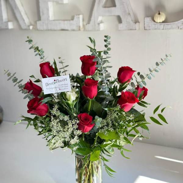 Red roses arranged in a clear glass vase with greenery