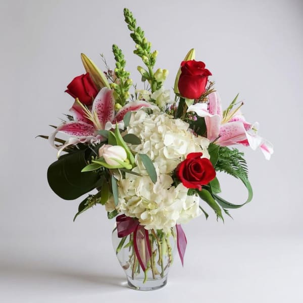 Red roses and pink lilies arranged with white hydrangea in a glass vase