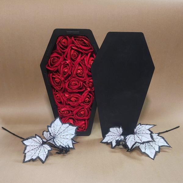 Black coffin-shaped box filled with red roses and white spiderweb leaves