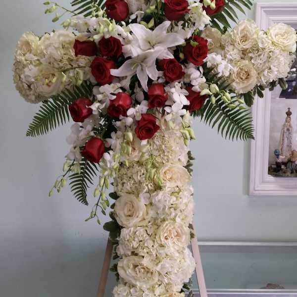 Cross-shaped floral arrangement with red roses and white blooms on an easel