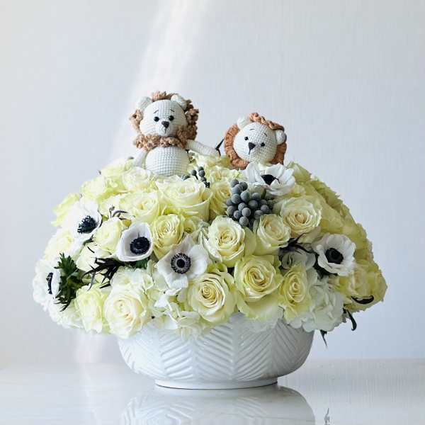 White rose arrangement in a textured bowl with two crocheted lion figures