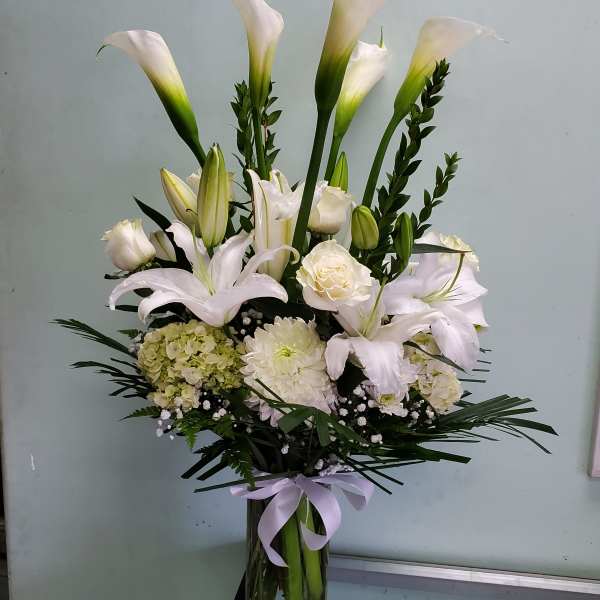 White calla lilies and roses arranged in a glass vase with a lavender ribbon